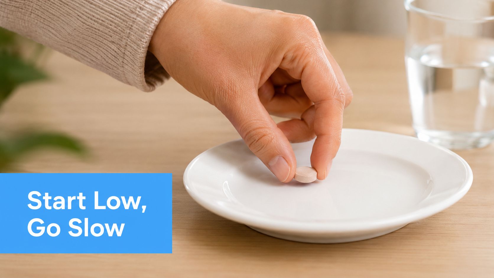 A hand placing a single small round pill onto a white plate with a glass of water nearby.
