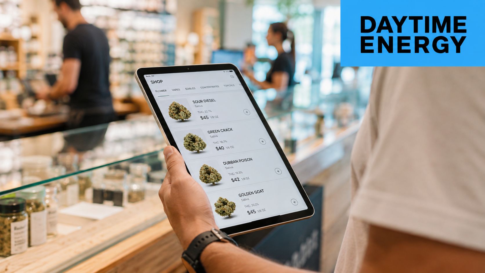 A customer choosing cannabis products on a digital tablet at a modern dispensary with staff in background.